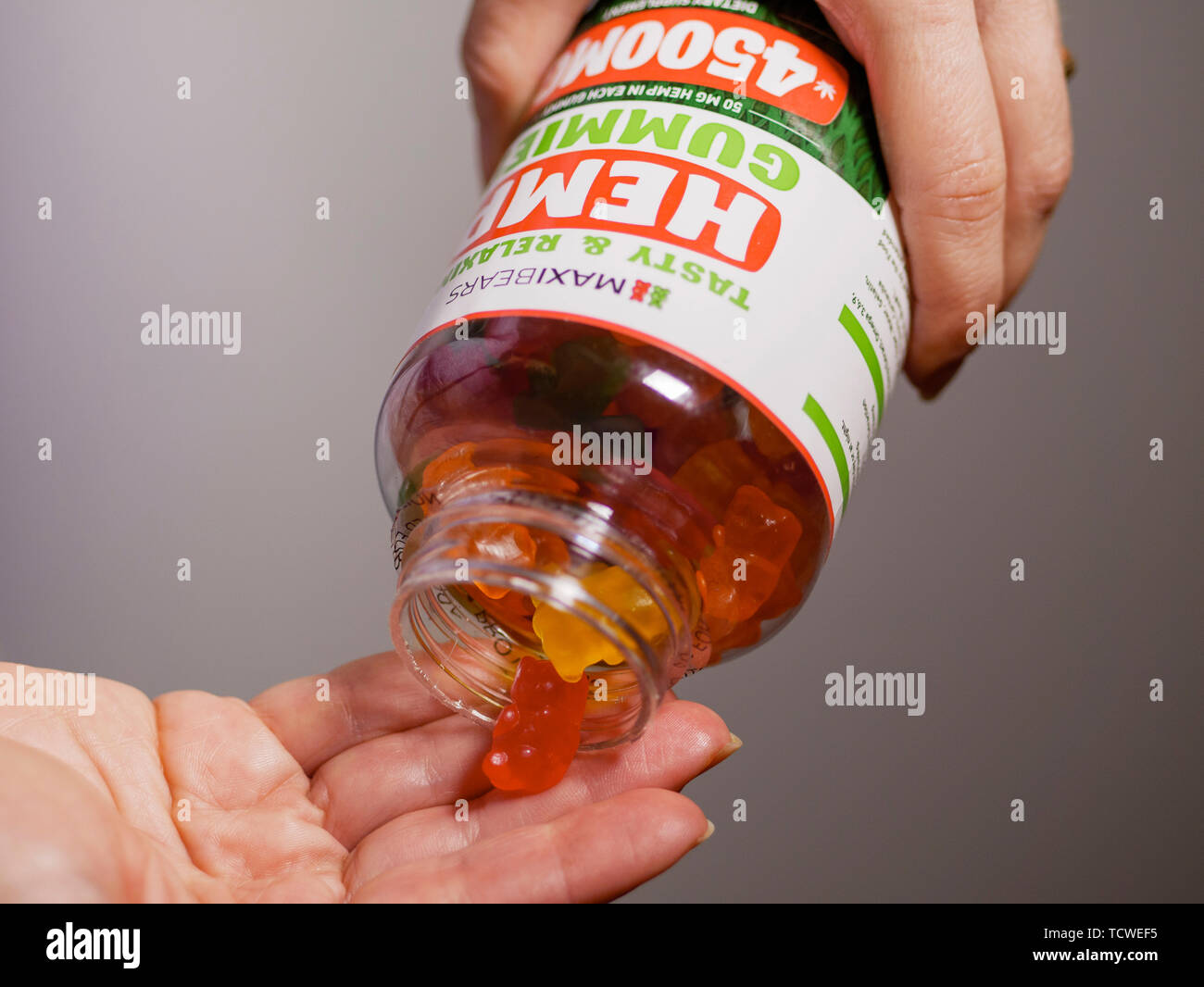 Hands dispensing CBD hemp oil gummies from bottle. Stock Photo