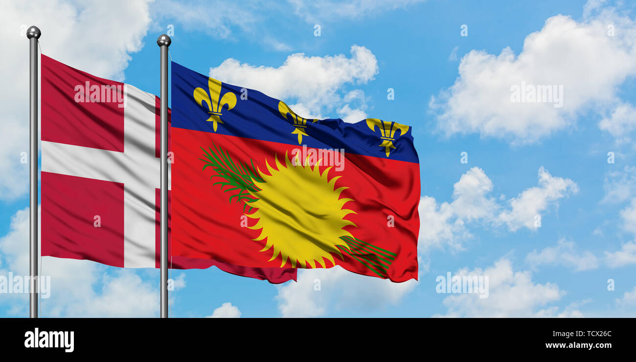 Denmark and Guadeloupe flag waving in the wind against white cloudy blue sky together. Diplomacy concept, international relations. Stock Photo