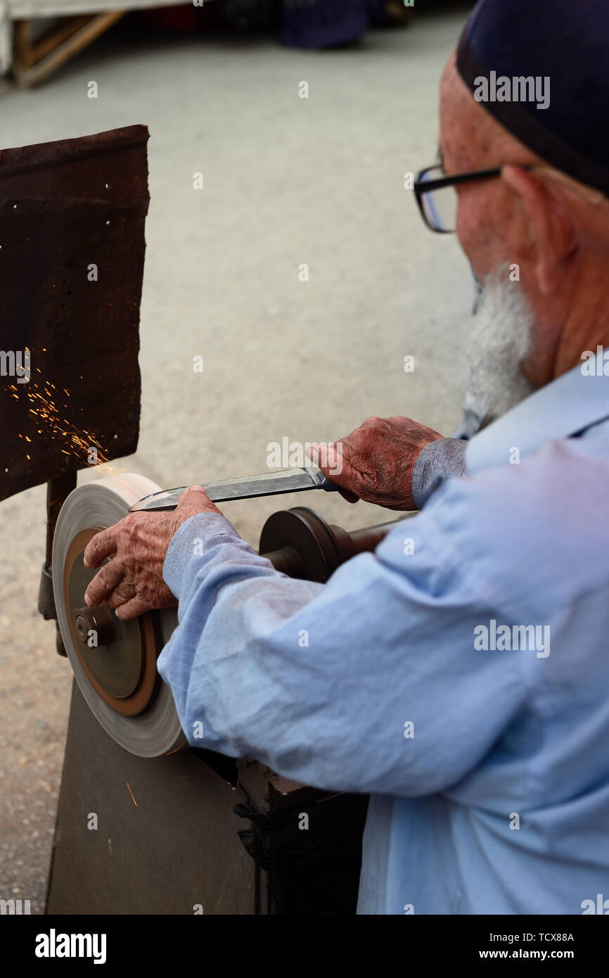 The man is sharpening traditional Uzbek knives on the street, Kokand bazaar. Stock Photo