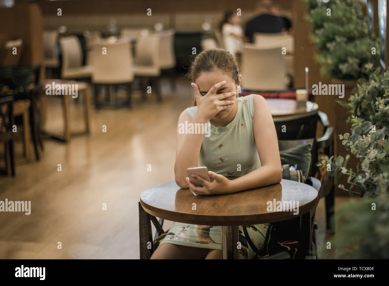 Young girl is crying along in cafe closing her face with her hand