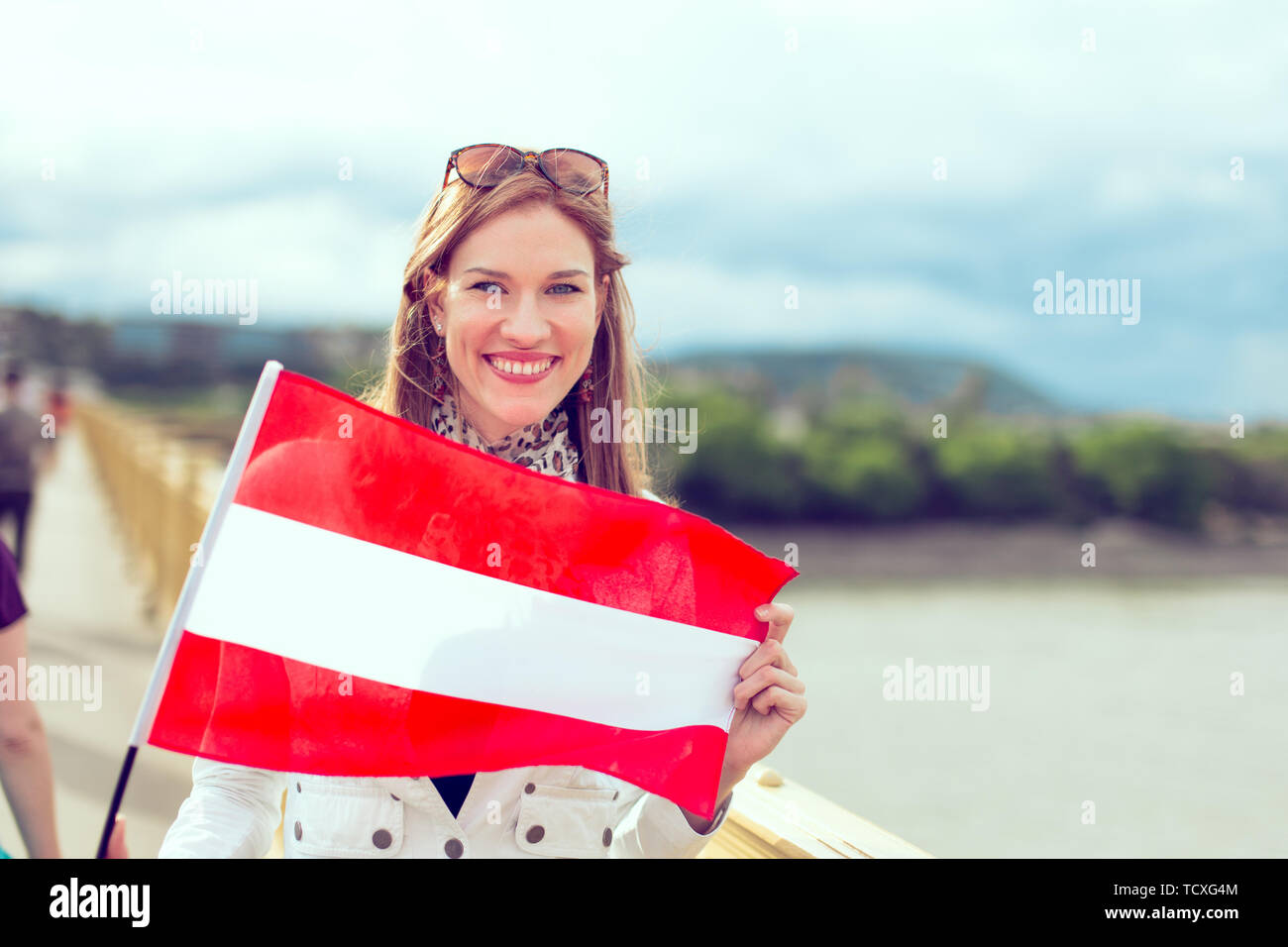 Happy young woman holding flag of Austria with toothy smile, outdoors, color graded Stock Photo