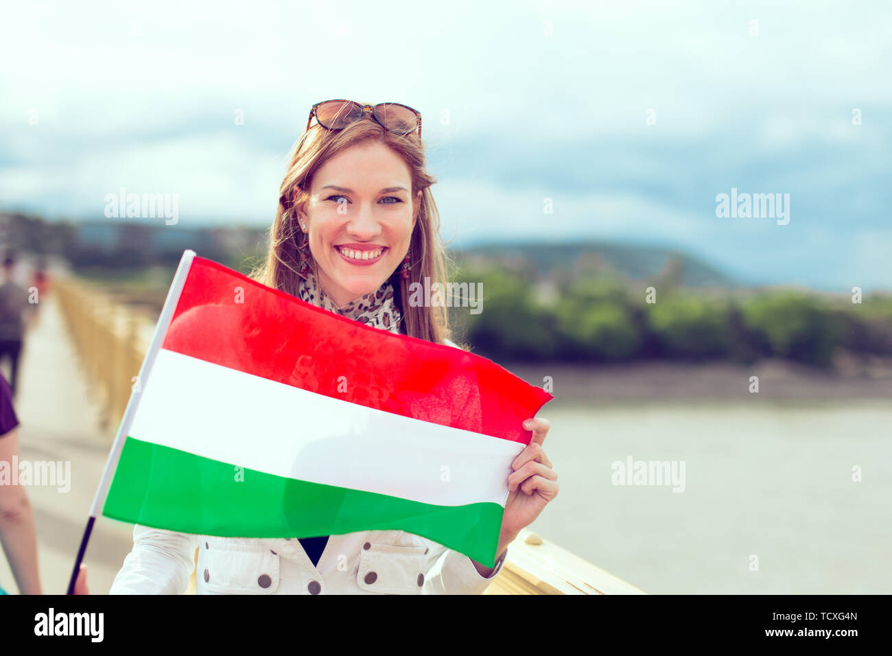 Happy young woman holding flag of Hungary with toothy smile, outdoors, color graded Stock Photo