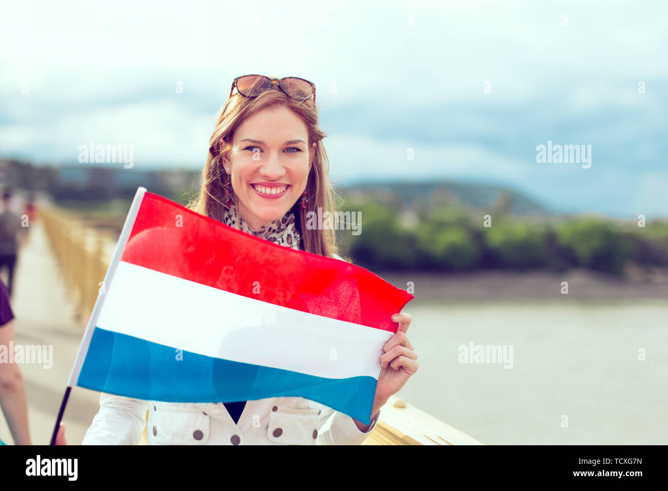 Happy young woman holding Dutch flag with toothy smile, outdoors, color graded Stock Photo