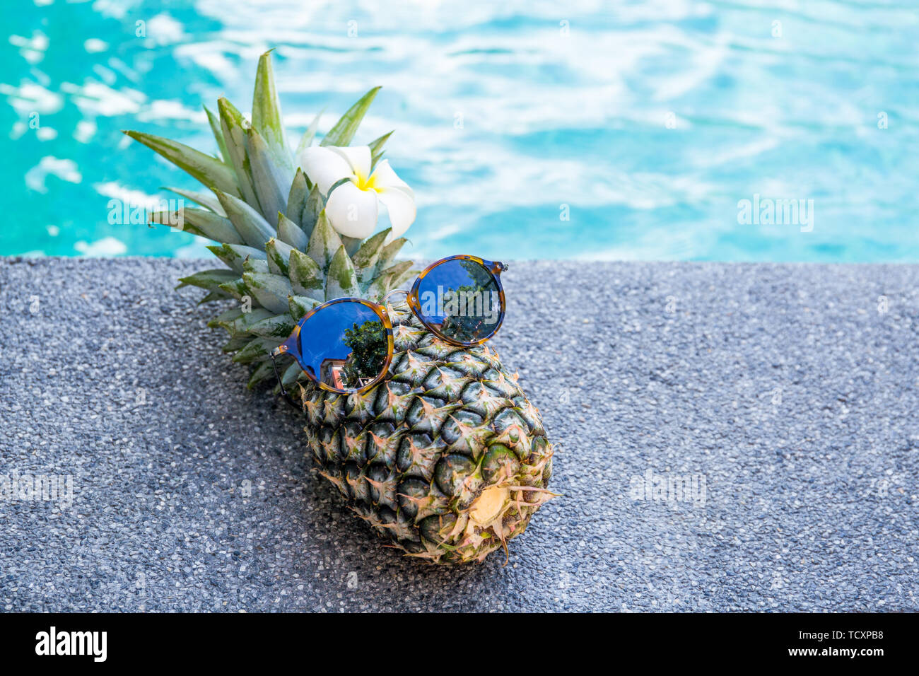 Summer concept funny pineapple wearing sunglasses beside swimming pool. Stock Photo