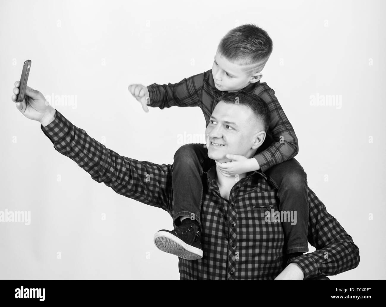 Taking selfie with son. Child riding on dads shoulders. Happiness being father of boy. Having fun. Fathers day. Father example of noble human. Father little son red shirts family look outfit. Stock Photo