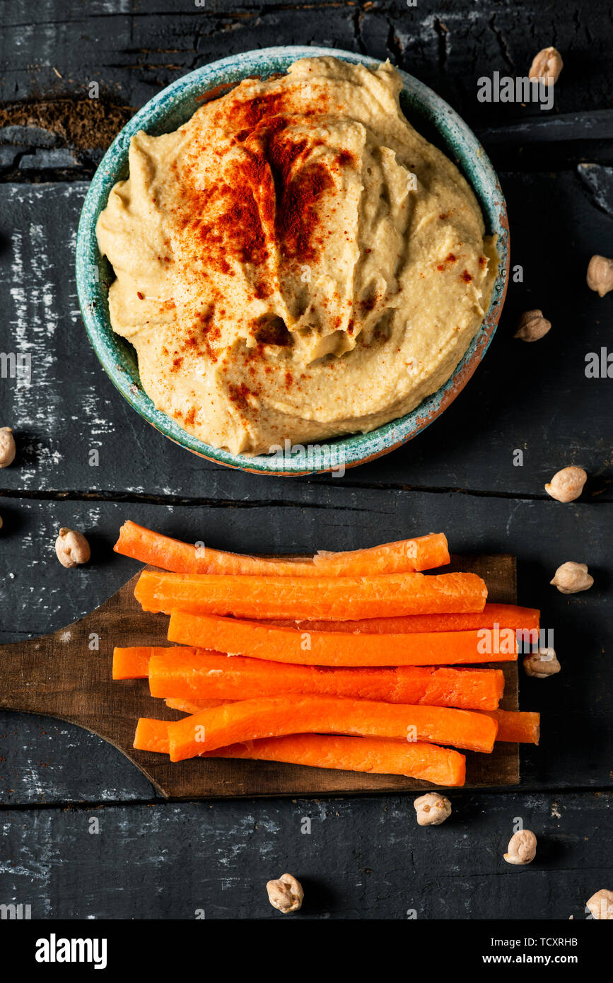 high angle view of a homemade hummus seasoned with paprika served in a green ceramic plate and some strips of carrot, to dip in it, on a dark gray rus Stock Photo