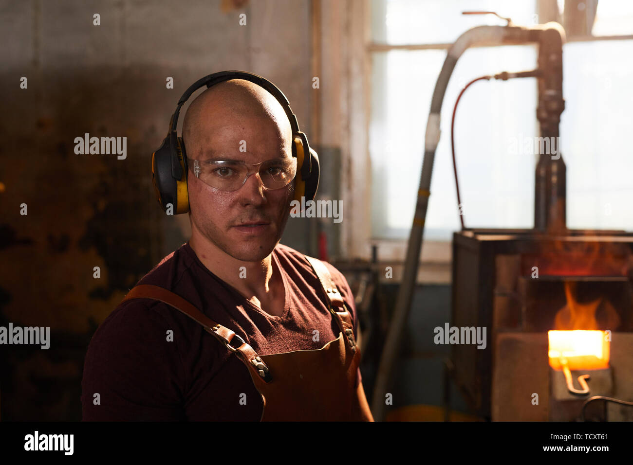Portrait of serious dirty bald blacksmith wearing ear protectors and safety goggles in workshop Stock Photo