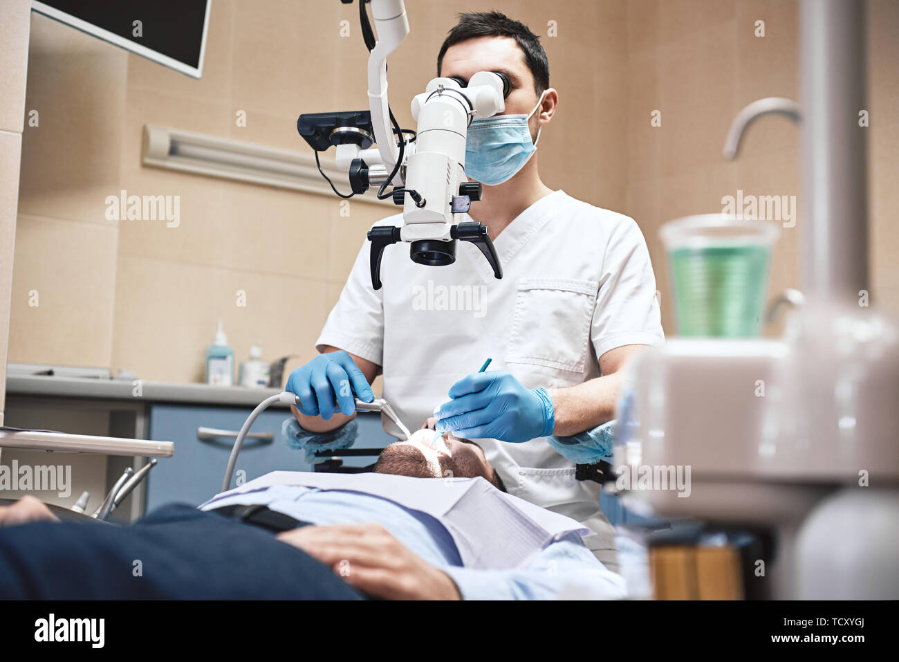 Male dentist wearing white uniform, looking into professional dental