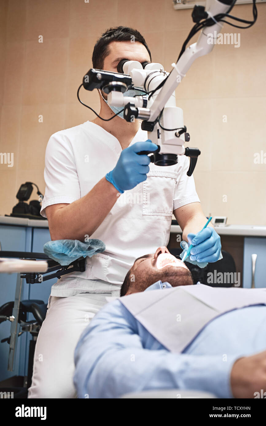 Male dentist wearing white uniform, looking into professional dental