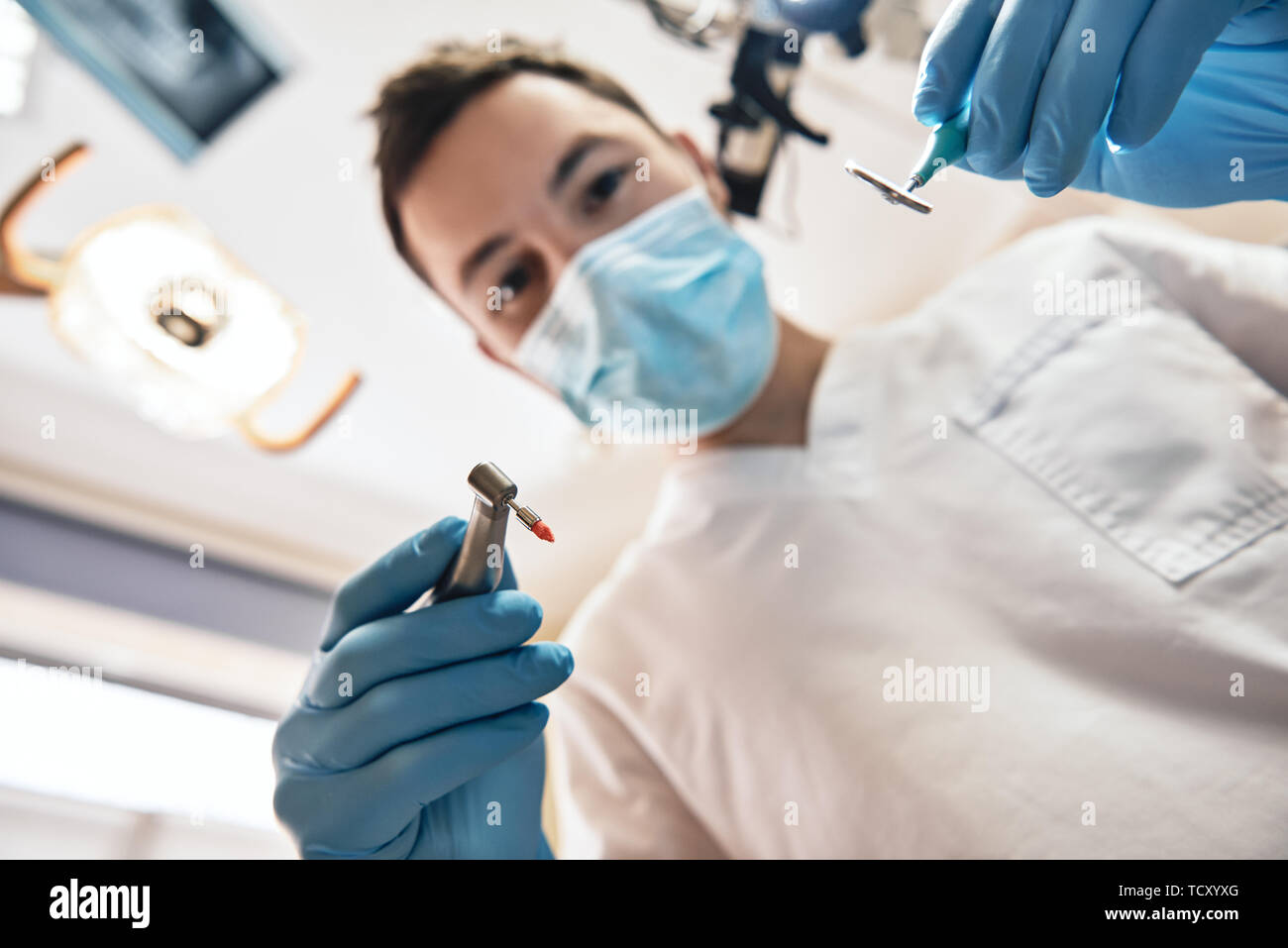 Young dentist is treating caries. He is standing and holding drill and