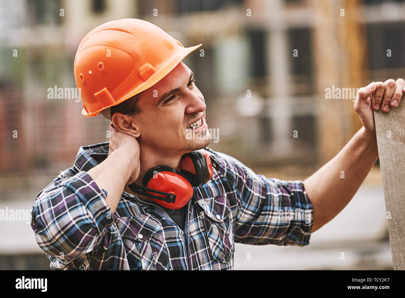 Be careful. Construction worker in protective helmet feeling neck pain while working at construction site. Building construction. Pain concept. Danger Stock Photo
