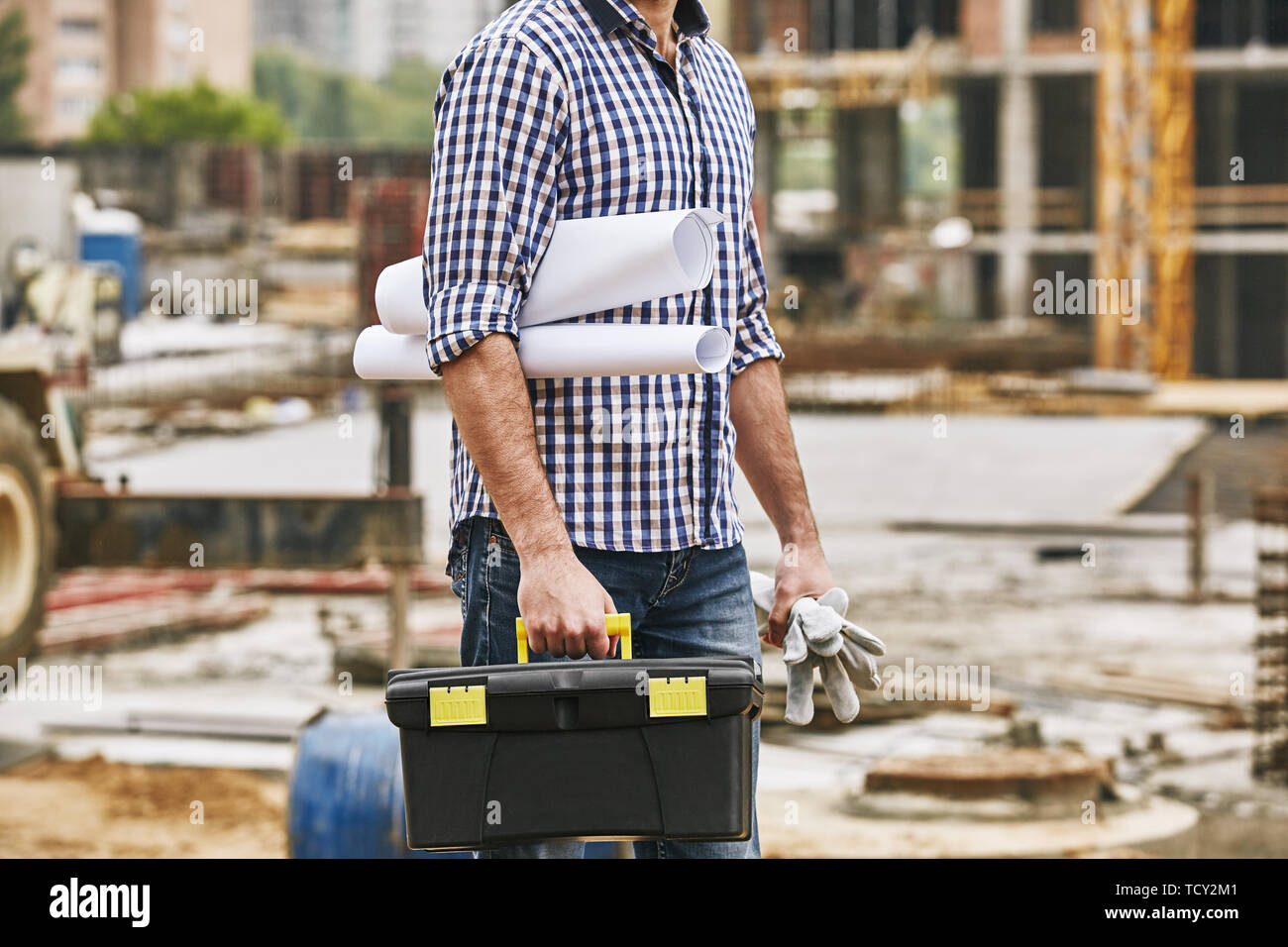 Everything what i need for work. Cropped image of a builder holding toolbox, protectives gloves and engineering drawings while standing at constructio Stock Photo