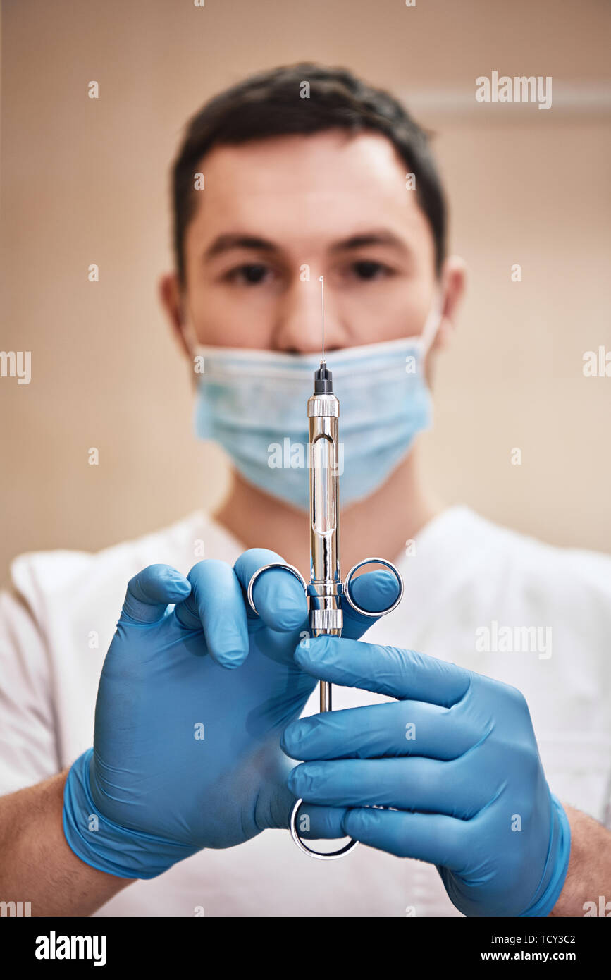 Male doctor with injection. Young dentist prepares a syringe for an