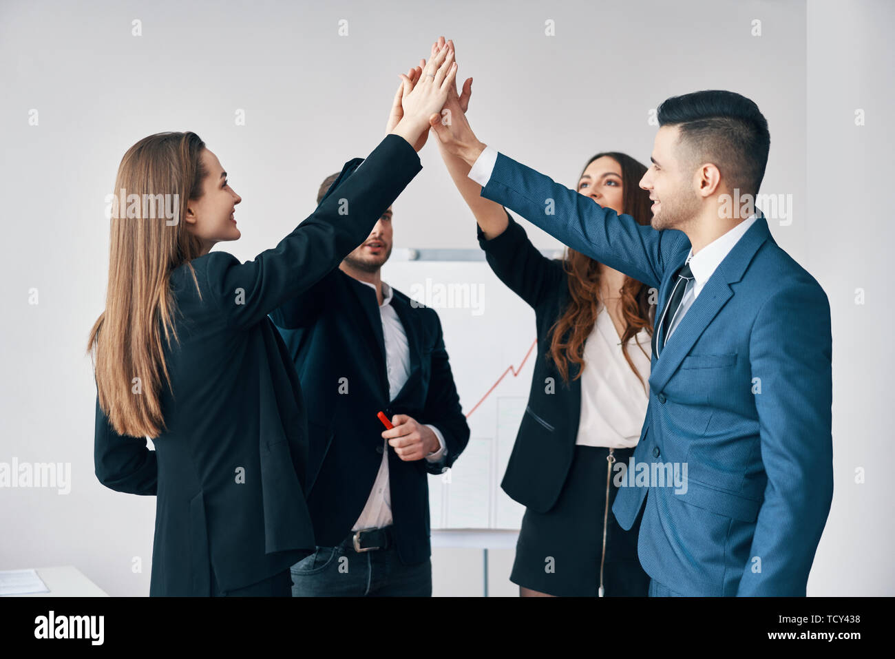 Smiling young business people giving high five to each other in office ...