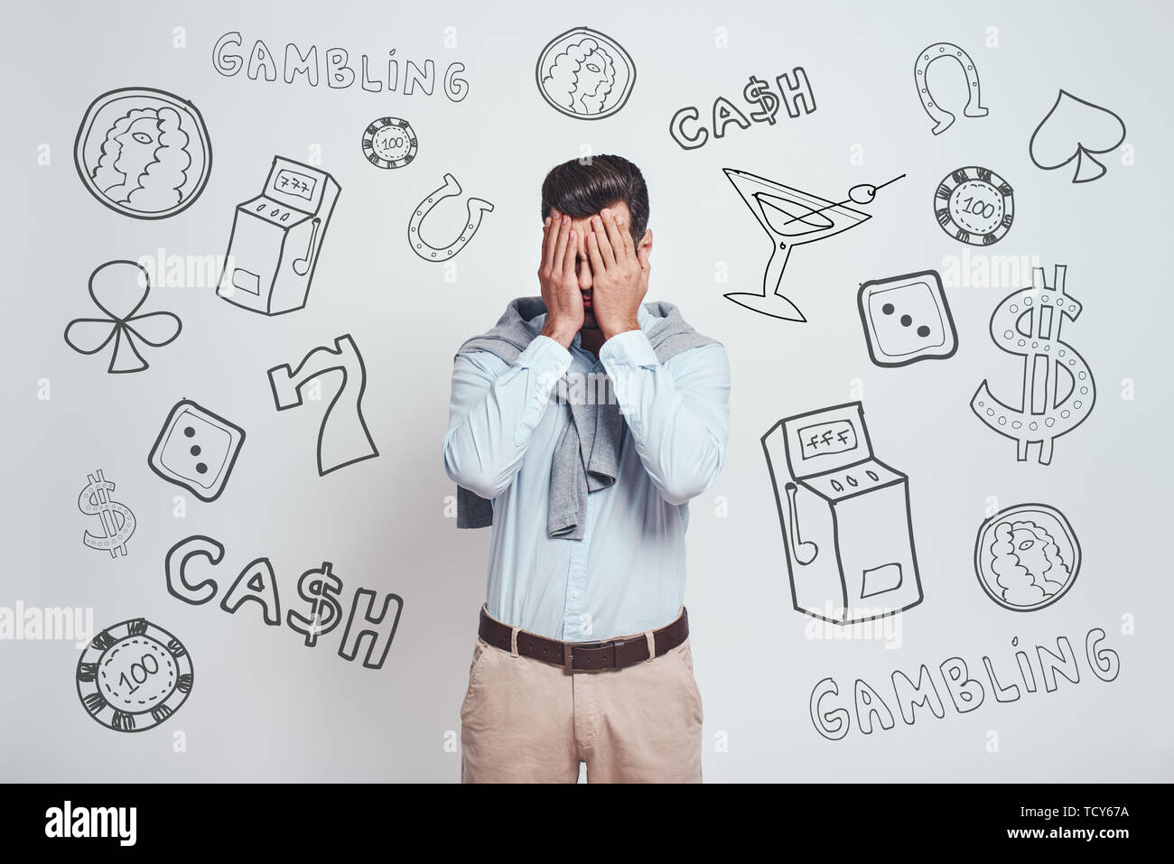 It is not my day. Depressed man in formal wear covering eyes with hands while standing against grey background with different doodle illustrations on  Stock Photo