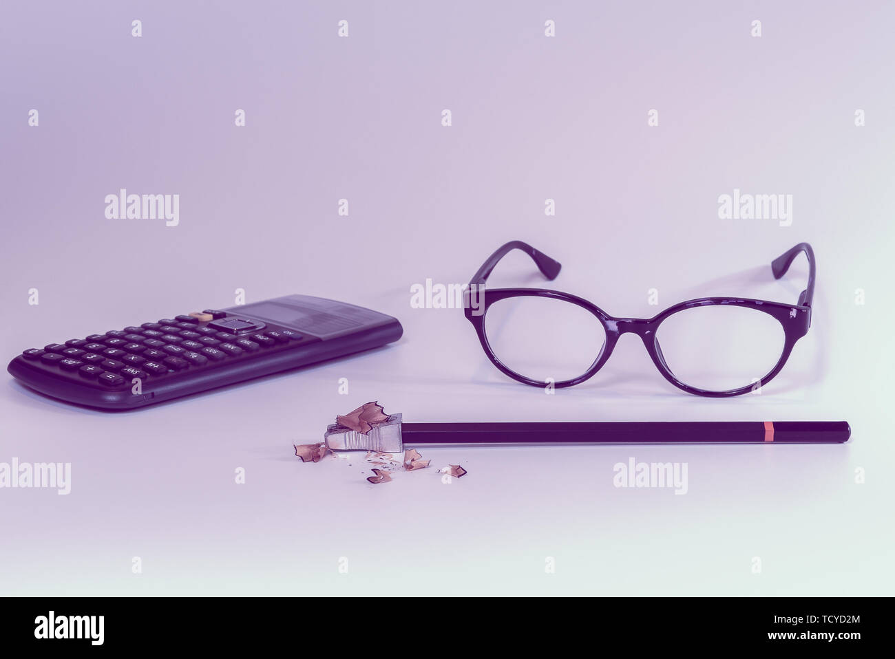 School or office supplies on a desk in feminine pink color with calculator, glasses, pencil and sharpener with wood shavings from sharpening Stock Photo