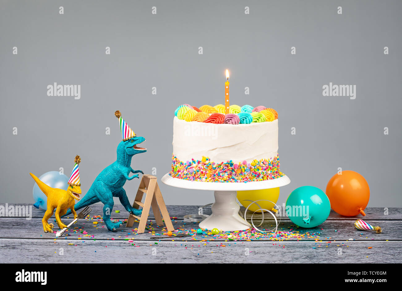 Hungry toy dinosaurs wearing hats and holding forks next to a birthday