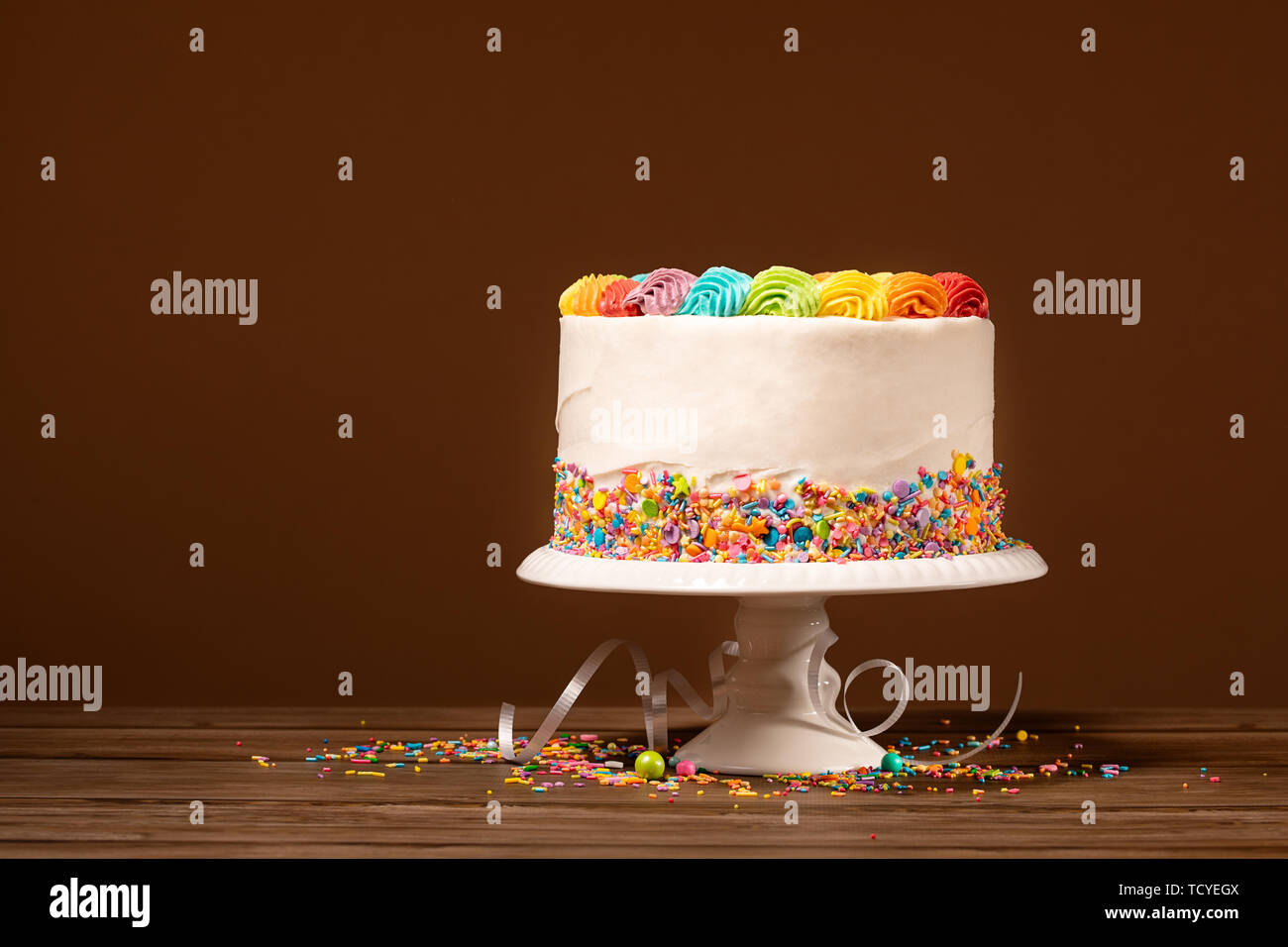 Birthday Cake With Rainbow Icing And Colorful Sprinkles Against A Brown Background Stock Photo Alamy