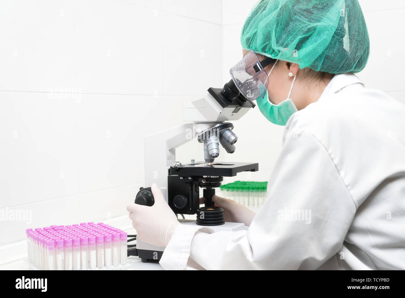 Young female scientist in modern laboratory, using microscope .  Stock Photo