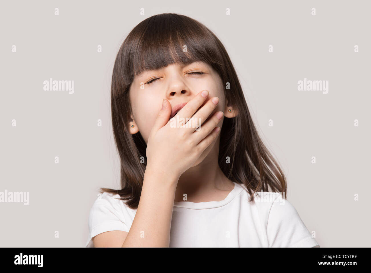 Little girl yawning feels sleepy isolated on beige studio background Stock Photo
