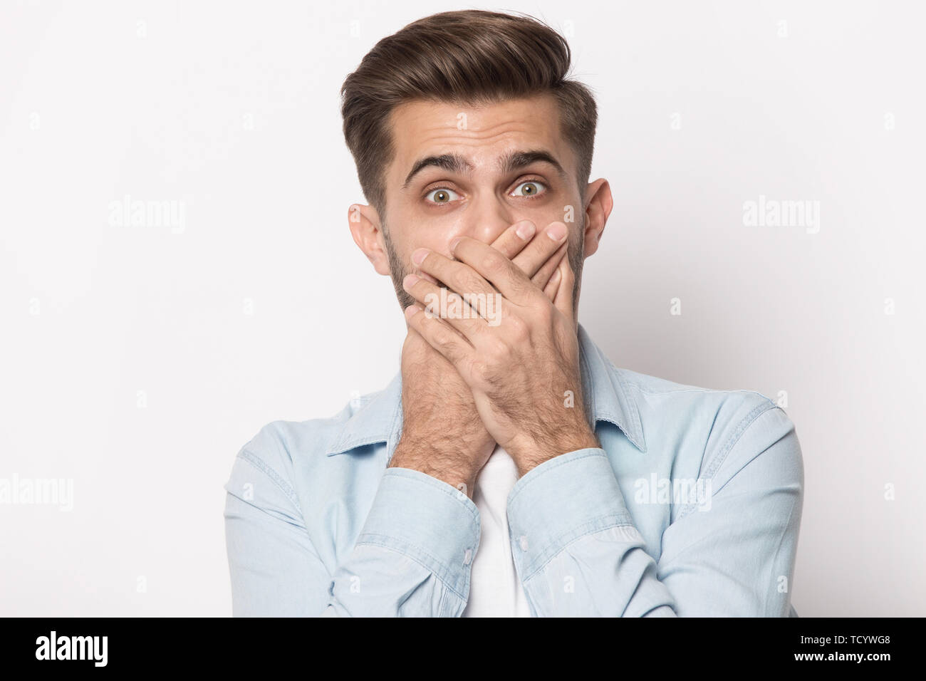 Horrified man covering mouth with hands looking at camera Stock Photo