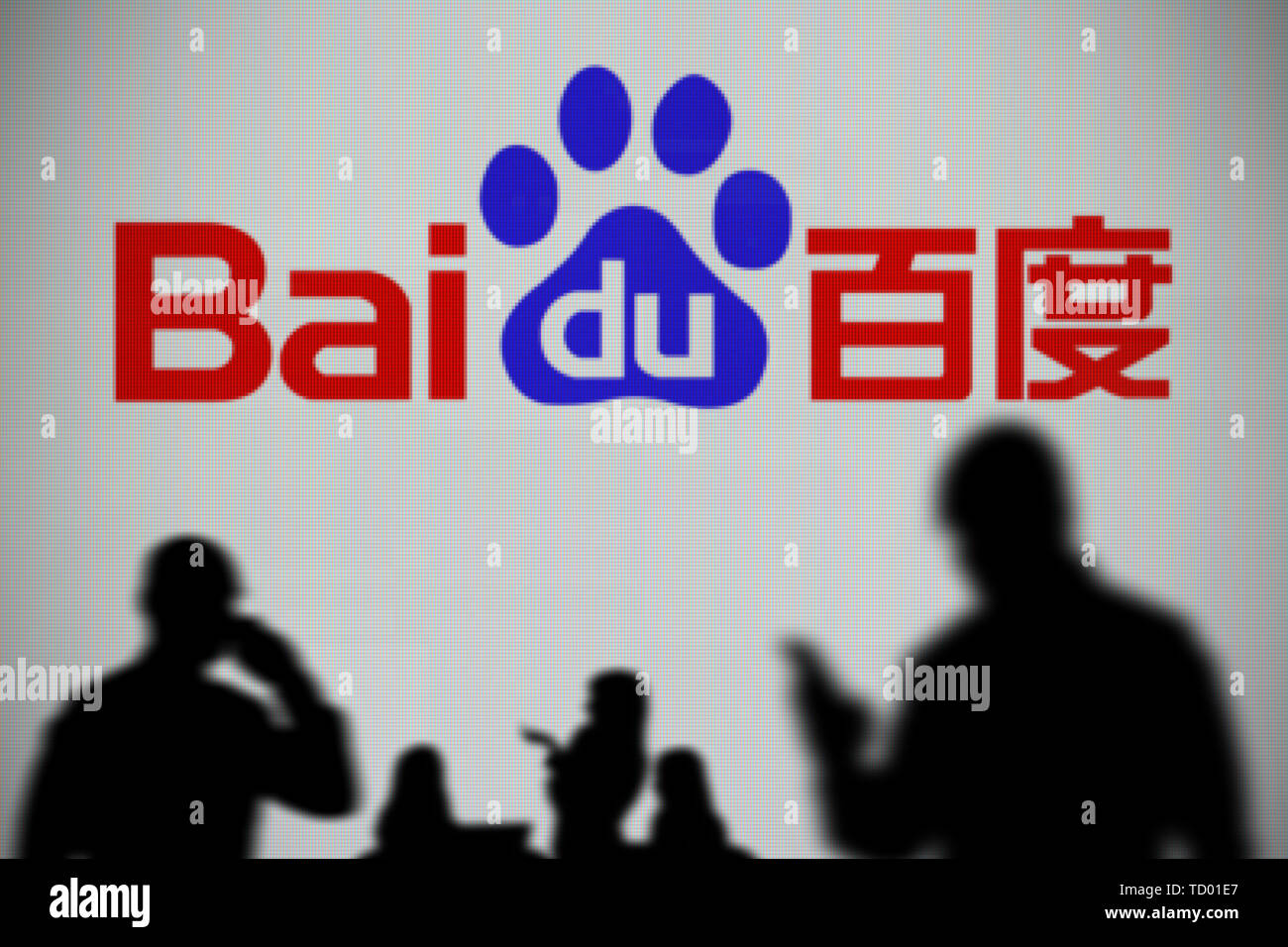 The Baidu logo is seen on an LED screen in the background while a silhouetted person uses a smartphone in the foreground (Editorial use only) Stock Photo
