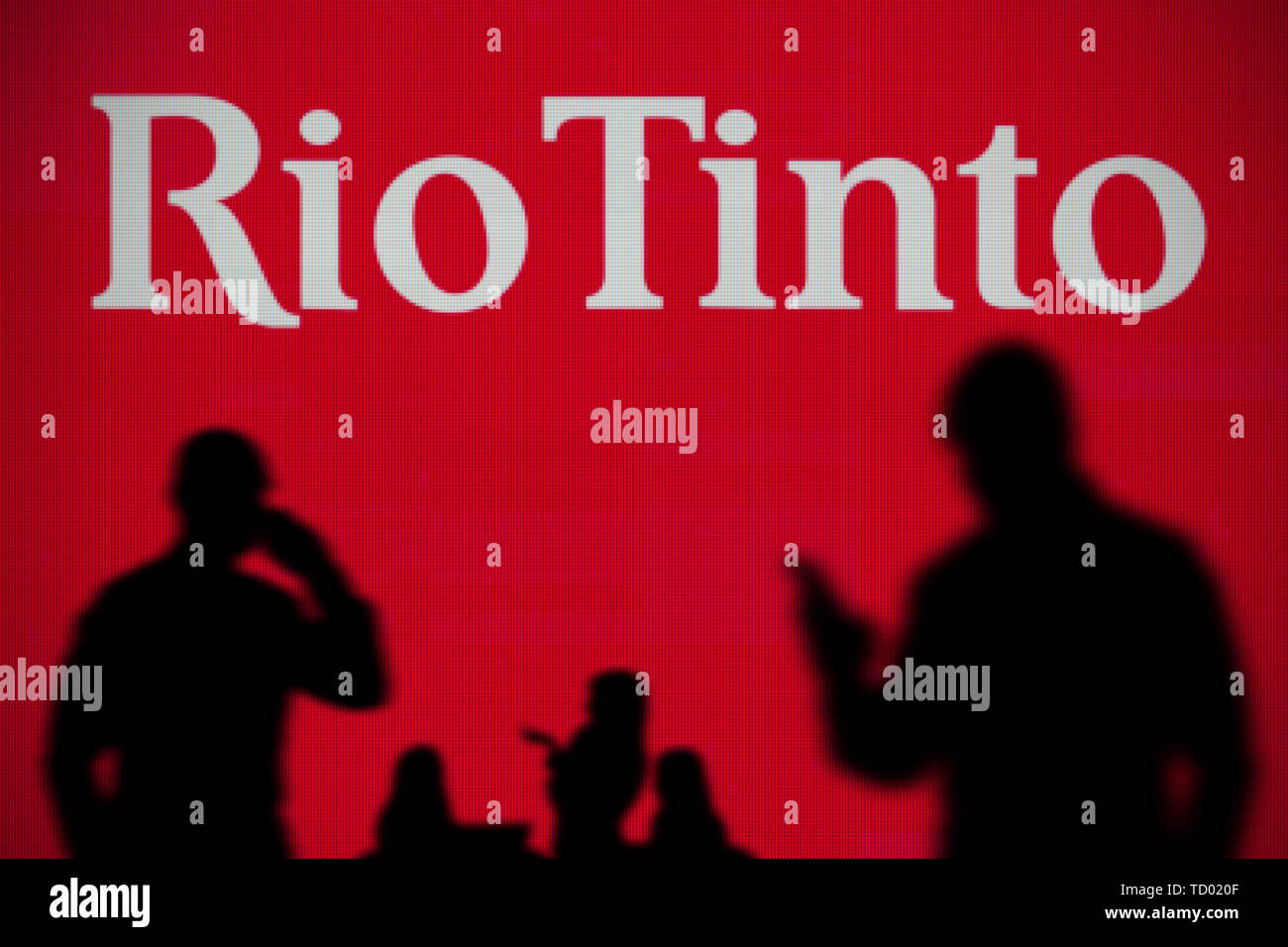 The Rio Tinto logo is seen on an LED screen in the background while a silhouetted person uses a smartphone in the foreground (Editorial use only) Stock Photo