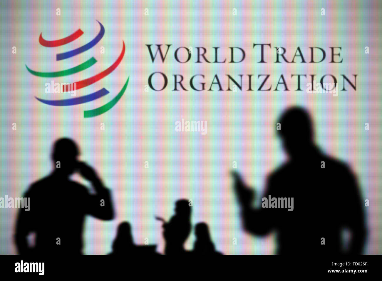 The World Trade Organization logo is seen on an LED screen in the while a silhouetted person uses a smartphone in the foreground (Editorial use only) Stock Photo