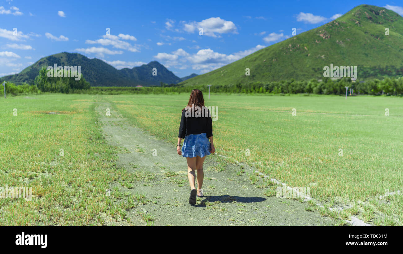 In the spring and summer beautiful nature, the mountains, and the blue sky, the clouds and the green grass underground, the girls traveling on the green outings, relaxing, leisure travel. Stock Photo