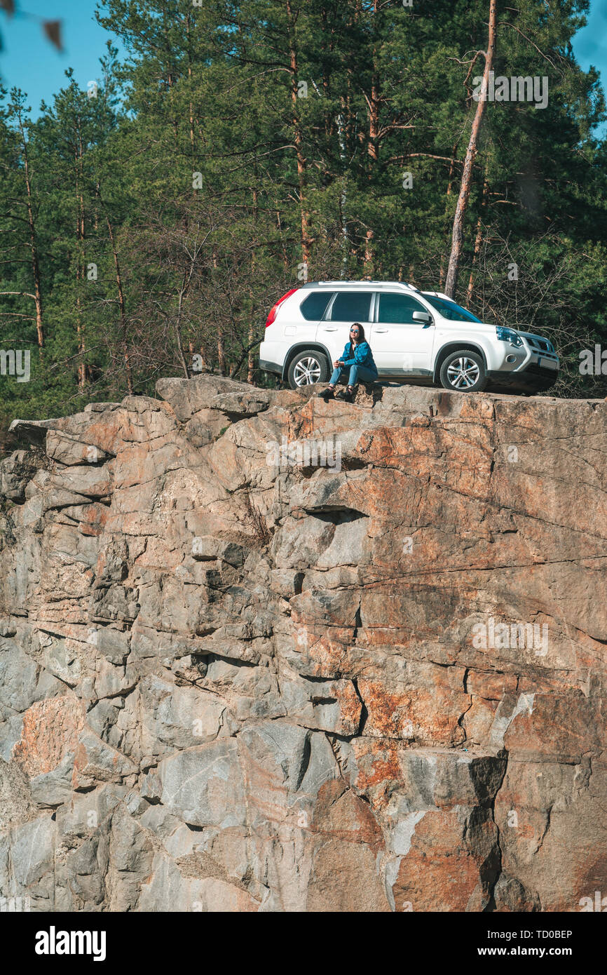 woman sitting on cliff with beautiful view at sunny day. suv car at background Stock Photo
