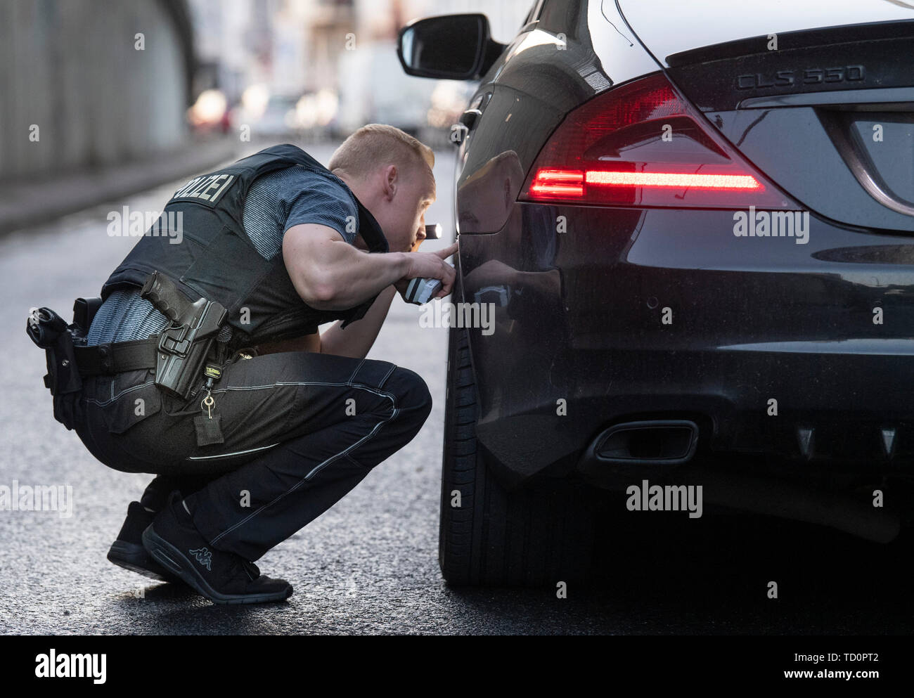 07 June 2019, Hessen, Frankfurt/Main: A police officer of the "Autoposer Raser Tuner Control Unit" (KART) uses a flashlight to check the rims of a Mercedes CLS 550 that had caught the attention of police officers in the city centre. The vehicle has been seized. (Zu dpa "Control unit KART on tour - expensive evening for Poser") Photo: Boris Roessler/dpa Stock Photo