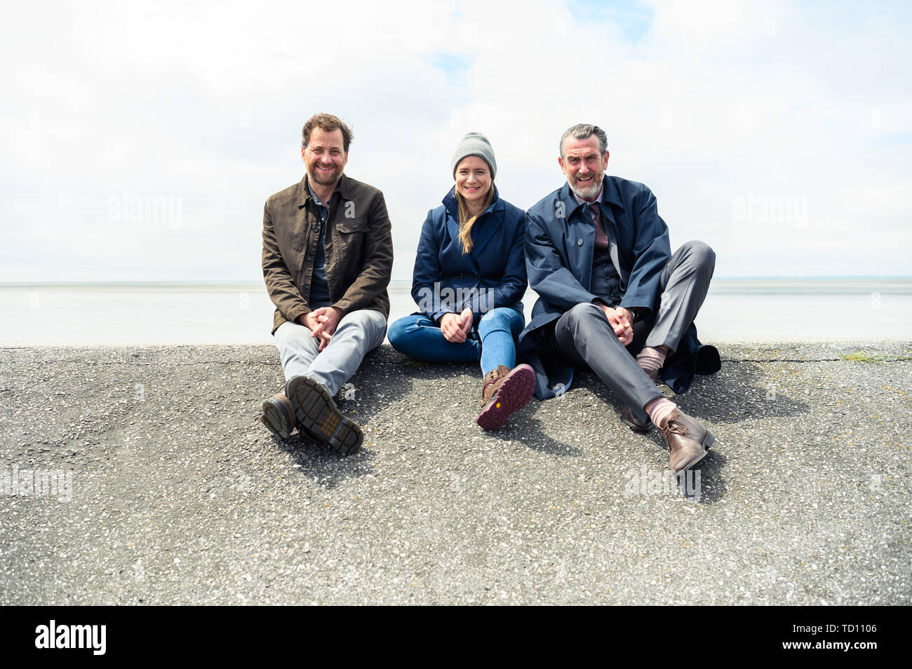 Norddeich, Germany. 11th June, 2019. Christian Erdmann (as Frank Eller; l-r), Julia Jentsch (as Ann Kathrin Klaasen), and Kai Maertens (as Ubbo Heide) sit on the dike during the press conference for the Saturday thriller 'Ostfriesengrab'. The fourth film in the Ostfriesland crime series is based on the novel of the same name by Klaus-Peter Wolf (about dpa 'successful author Klaus-Peter Wolf provides material for new ZDF crime thriller'). Credit: Mohssen Assanimoghaddam/dpa/Alamy Live News Stock Photo