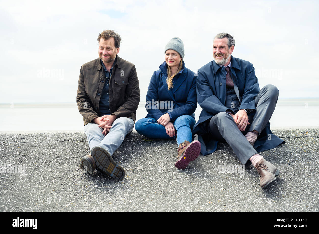 Norddeich, Germany. 11th June, 2019. Kai Maertens (as Ubbo Heide; l-r), Julia Jentsch (as Ann Kathrin Klaasen) and Christian Erdmann (as Frank Eller) sit on the dike during the press date for the Saturday thriller 'Ostfriesengrab'. The fourth film in the Ostfriesland crime series is based on the novel of the same name by Klaus-Peter Wolf (about dpa 'successful author Klaus-Peter Wolf provides material for new ZDF crime thriller'). Credit: Mohssen Assanimoghaddam/dpa/Alamy Live News Stock Photo