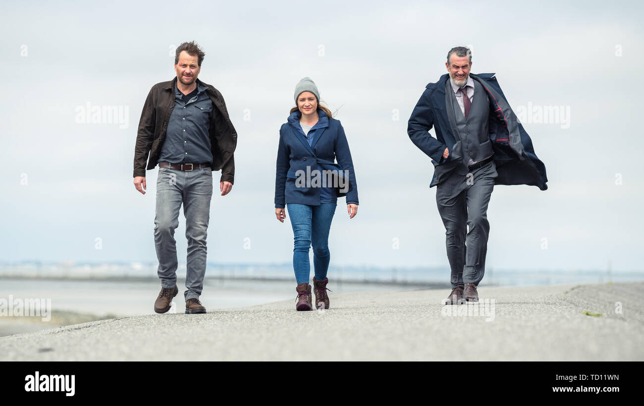 Norddeich, Germany. 11th June, 2019. Christian Erdmann (as Frank Eller; l-r), Julia Jentsch (as Ann Kathrin Klaasen), and Kai Maertens (as Ubbo Heide) walk along the dike during the press conference to the Saturday thriller 'Ostfriesengrab'. The fourth film in the Ostfriesland crime series is based on the novel of the same name by Klaus-Peter Wolf (about dpa 'successful author Klaus-Peter Wolf provides material for new ZDF crime thriller'). Credit: Mohssen Assanimoghaddam/dpa/Alamy Live News Stock Photo