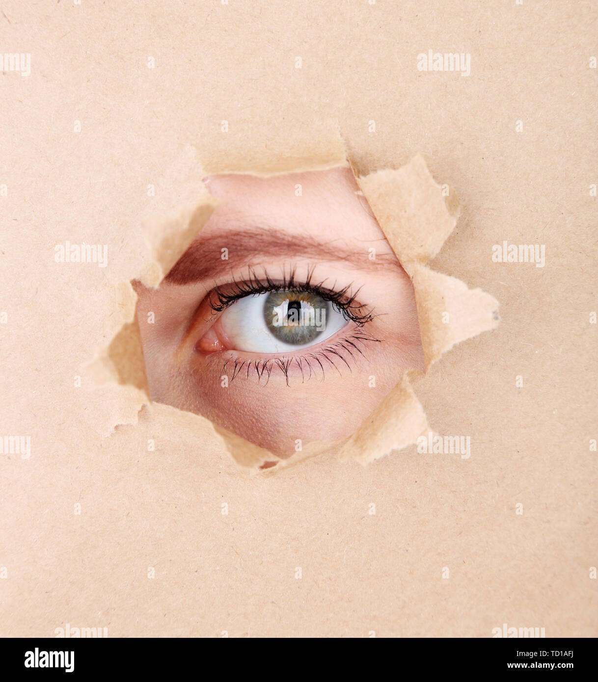 Female eye looking through hole in sheet of paper Stock Photo