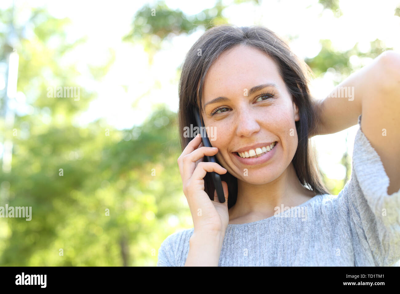 Happy woman calls on smart phone standing outdoors in a park Stock Photo