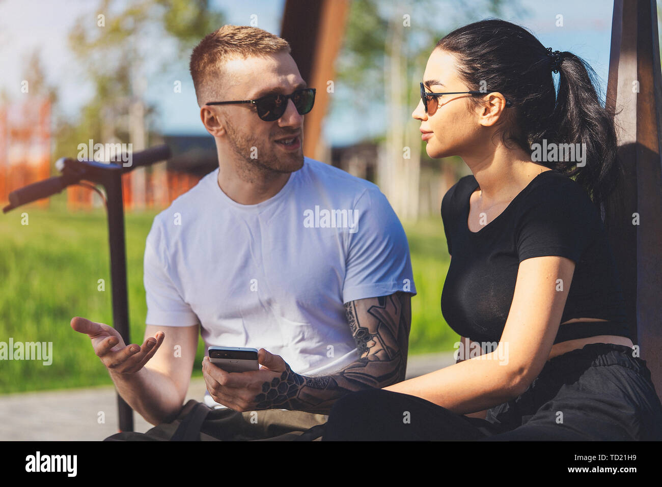 Couple of young man and woman sitting in park on wooden bench. Stock Photo