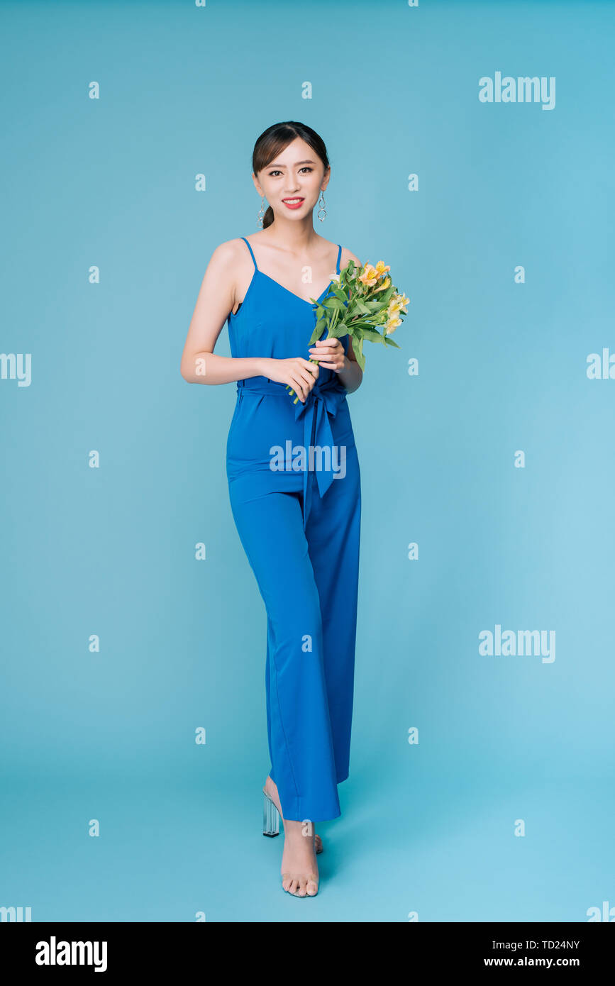 Beautiful girl in the blue dress with flowers in hands on a light ...