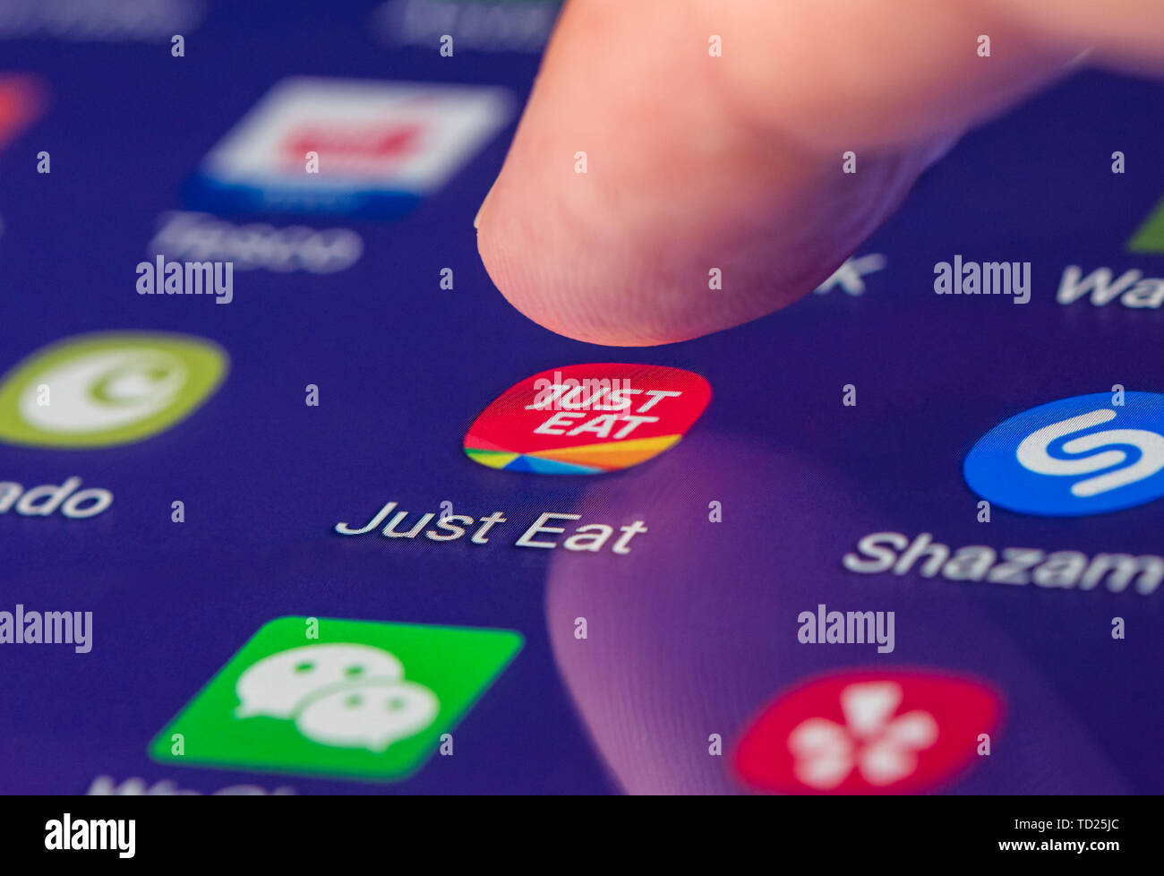 Finger pressing the Just Eat app icon on a touchscreen of a tablet or smartphone mobile device, to order fast food online. Stock Photo