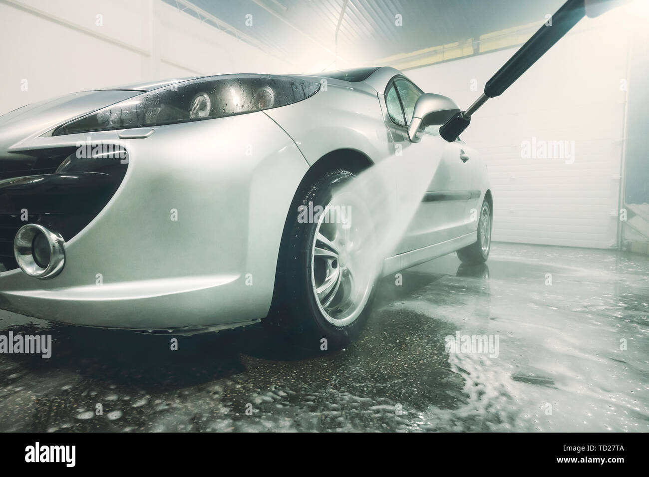 Man cleaning vehicle with high pressure water spray or jet. Car wash