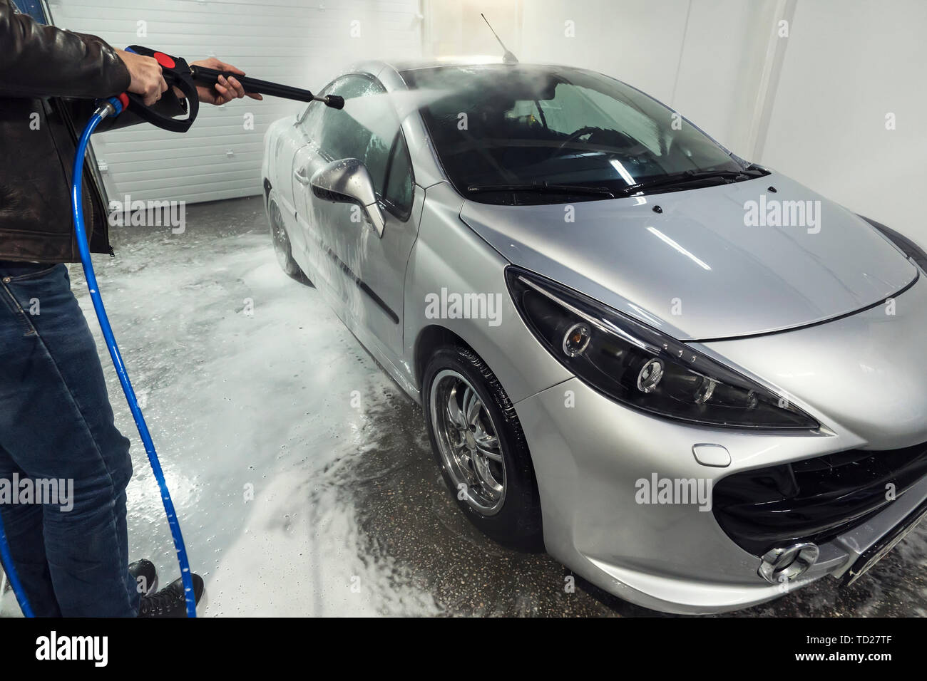 A man sprays foam on the car from a special spray. Car wash with foam