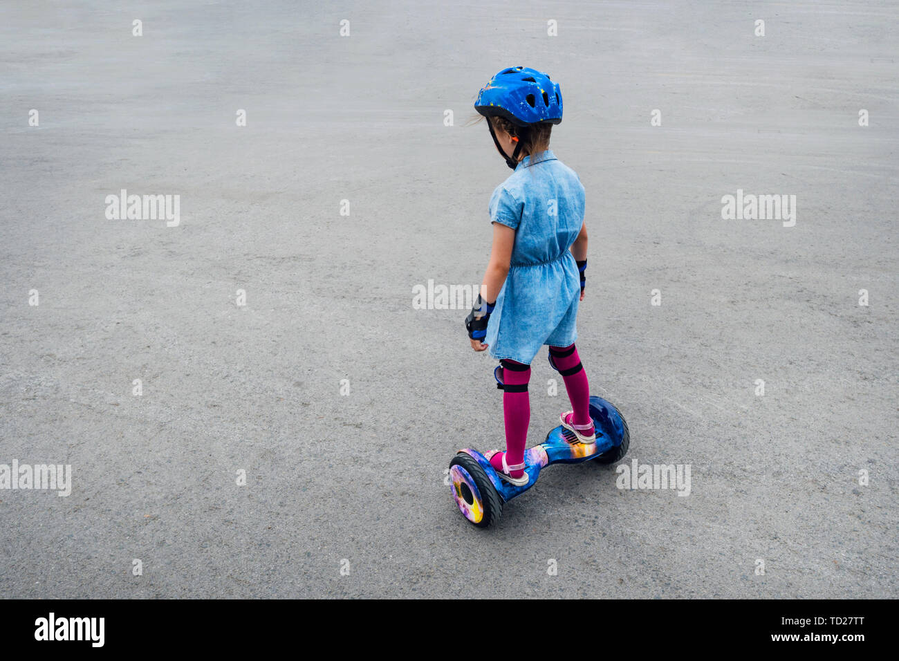 Happy girl riding on gyroscooter outdoors. Active life concept. Child rides on hover board in protective gear helmet knee pads elbow pads. Dangerous Stock Photo