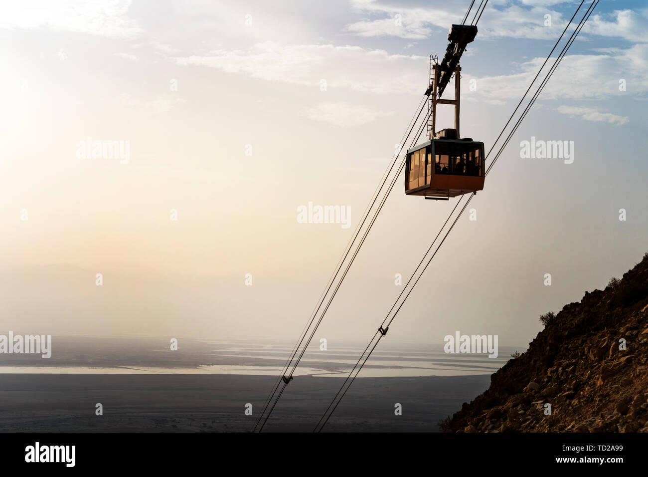 Cable car with people going down on funicular over mountains in Judean desert at the Dead sea background. Scenic view of the cable railroad with the Stock Photo
