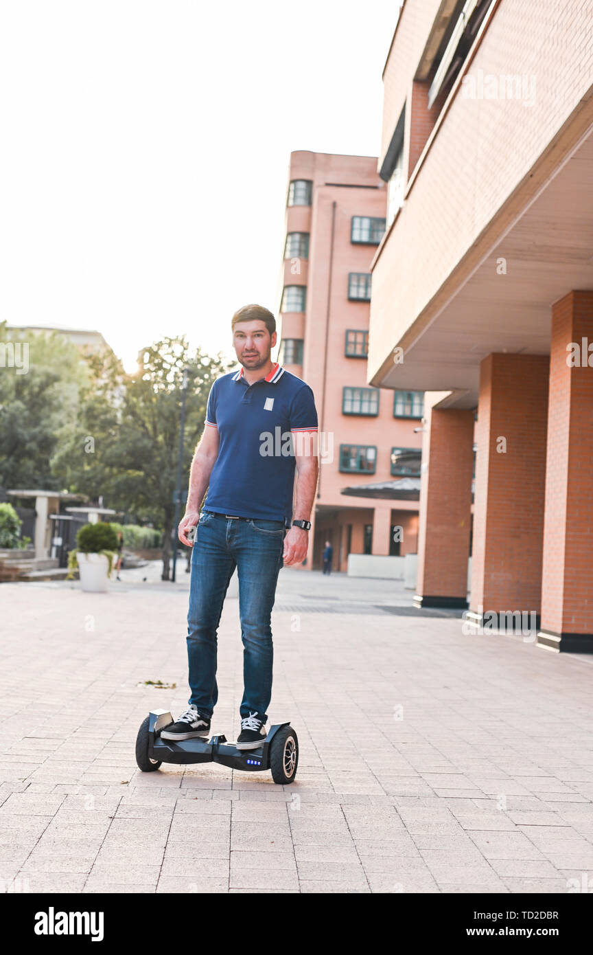 A man in jeans and sneakers on a hoverboard ride in the city. Happy boy riding around at sunset. Modern electronics for relaxation and entertainment Stock Photo