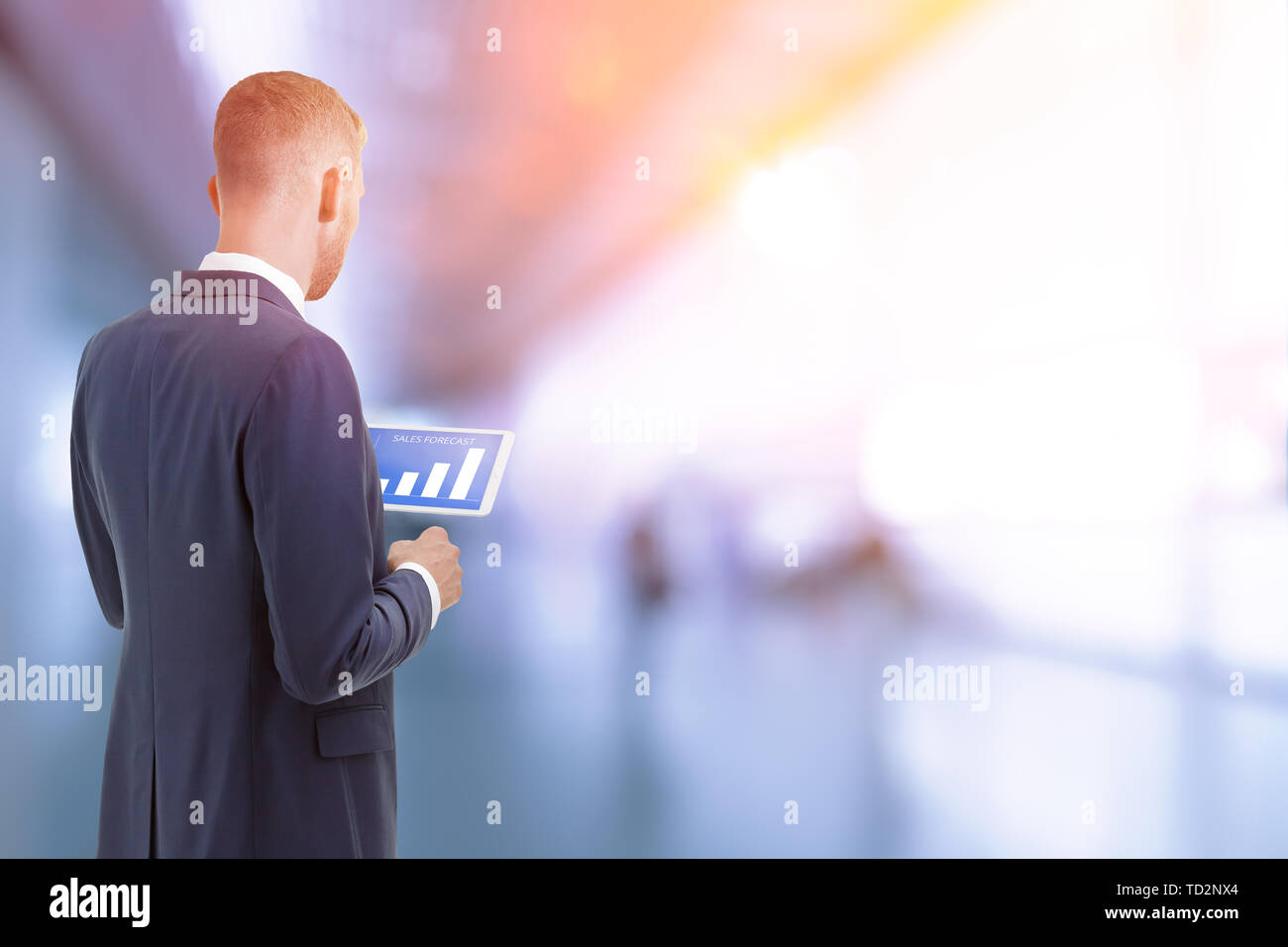 Man in suit inside an office building looking at sales forecast graphics on a tablet computer Stock Photo