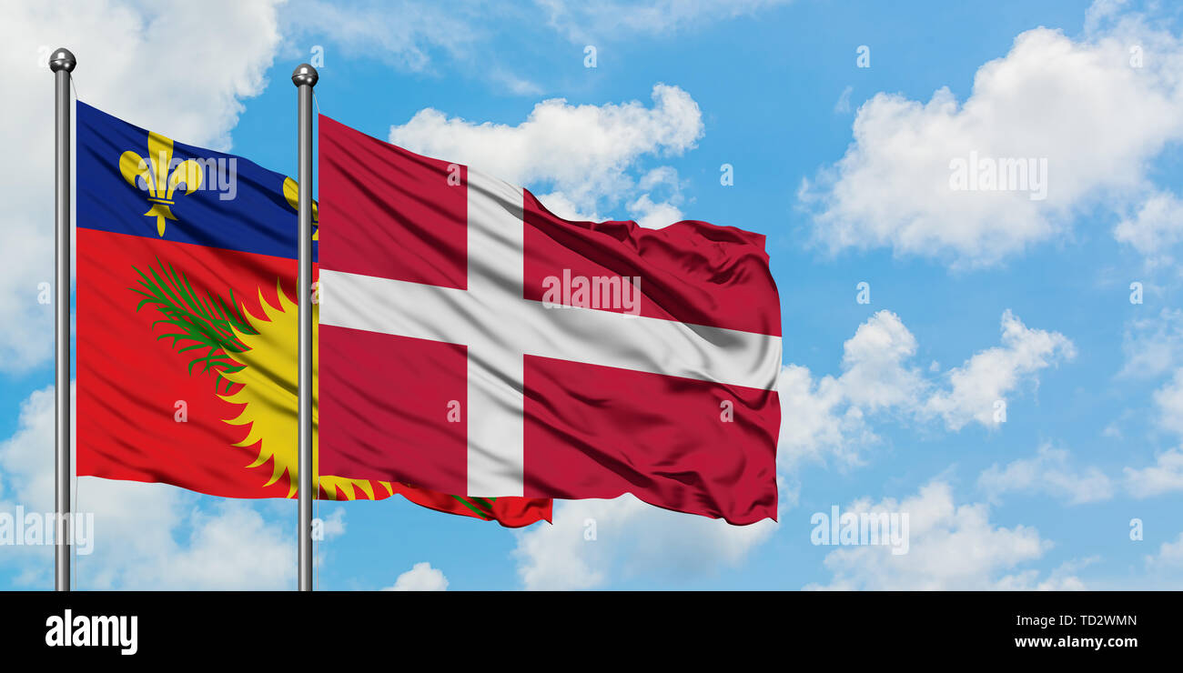 Guadeloupe and Denmark flag waving in the wind against white cloudy blue sky together. Diplomacy concept, international relations. Stock Photo