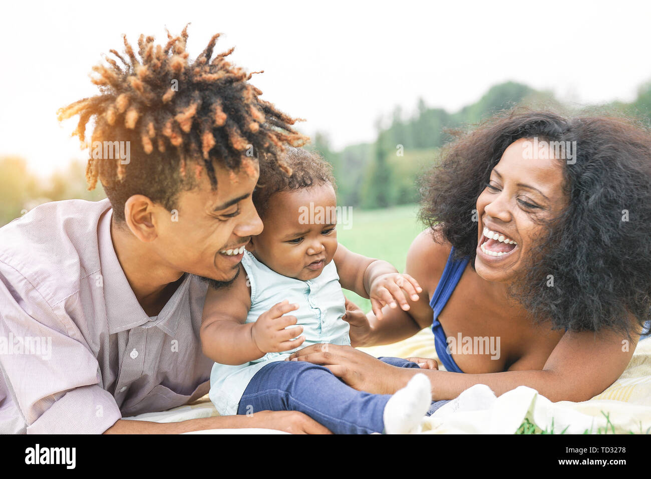 Happy African family enjoying a picnic sunny day outdoor - Mother and father having fun with their daughter in a public park Stock Photo