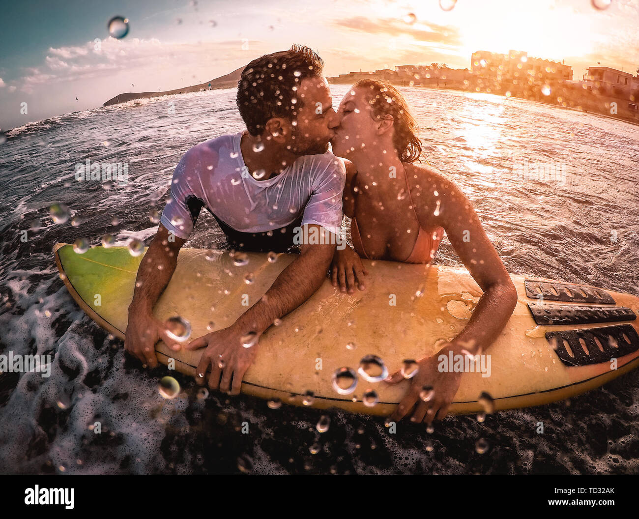 Happy romantic couple kissing while surfing in the ocean - Sporty surfers bodybording having a tender moment in the water Stock Photo
