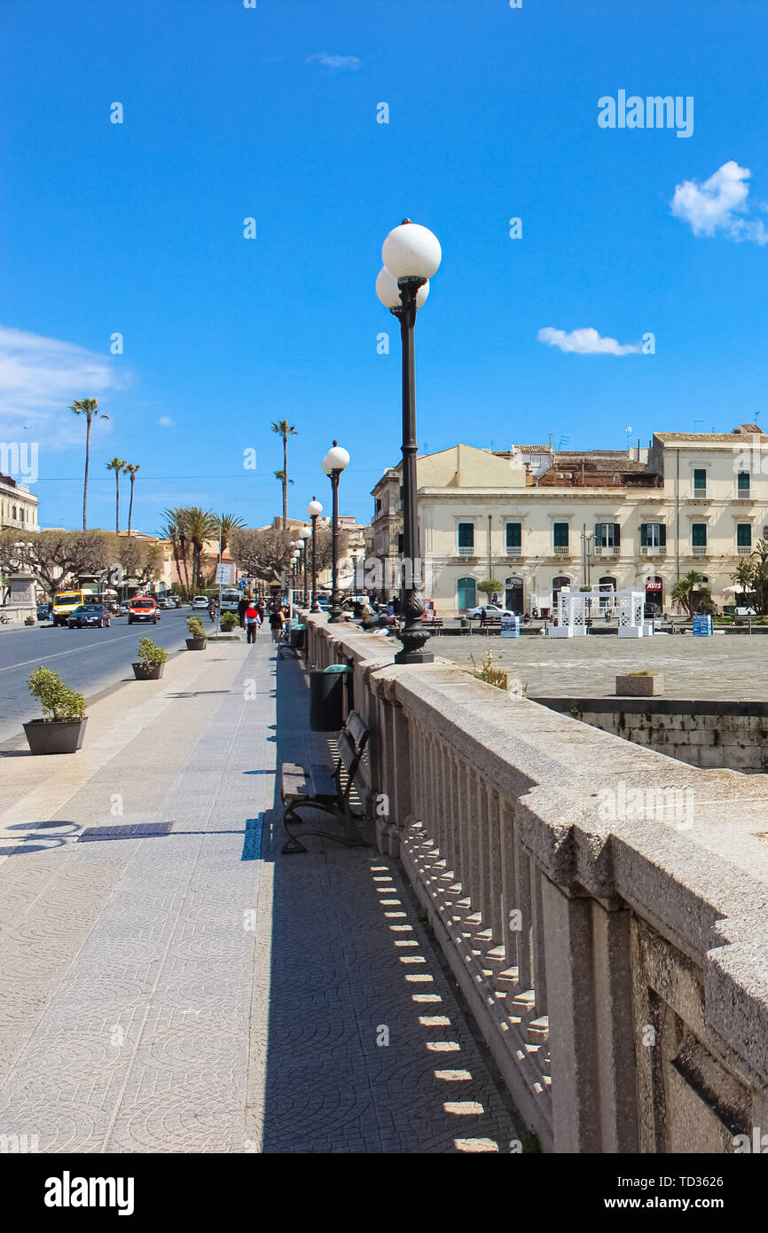 Syracuse, Sicily, Italy - Apr 10th 2019: Sidewalk on a bridge connecting Syracuse and Ortigia Island captured on a vertical photo with blue sky. Famous Ortygia is a popular tourist attraction. Stock Photo