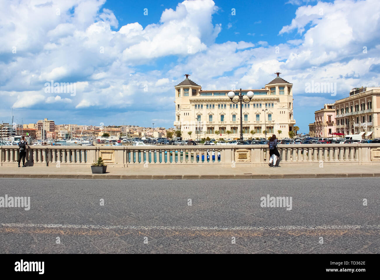 Syracuse, Sicily, Italy - Apr 10th 2019: Tourists standing on a bridge and taking pictures of a beautiful marina on a sunny day. The bridge is connecting Syracuse and famous Ortigia Island. Stock Photo